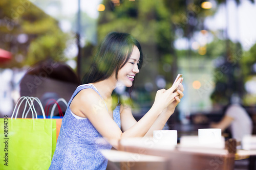 smiling young woman looking at smart phone in cafe shop