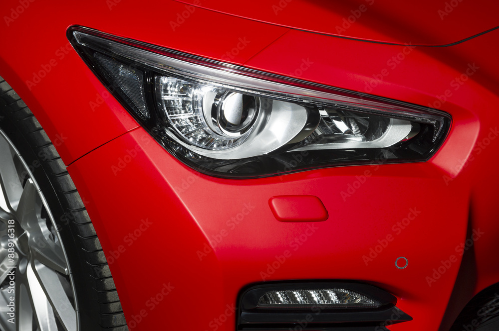 Predatory car headlight and hood of powerful sports car with matte red paint and wheel with silver disc 