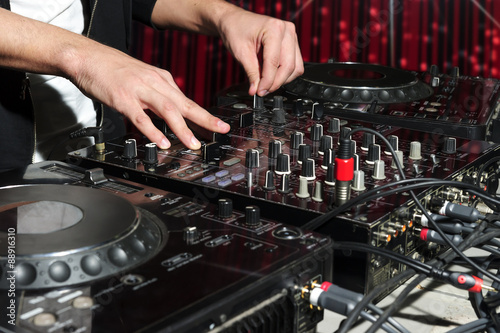 DJ at dance party mixes track on sound mixer, nightclub with striped red interior, professional stereo electronic equipment 