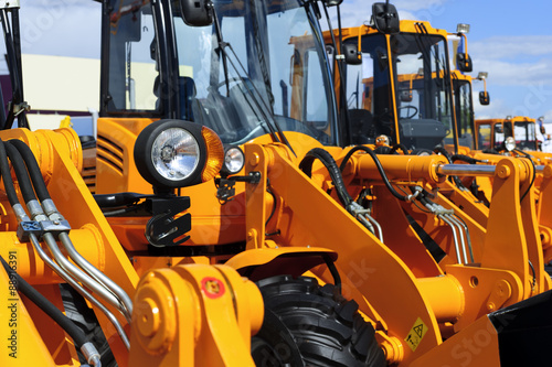 Bulldozer headlight, row of huge orange powerful construction machines, tractors, excavators, focused on spotlight, blue sky and white clouds on background, selective focus 