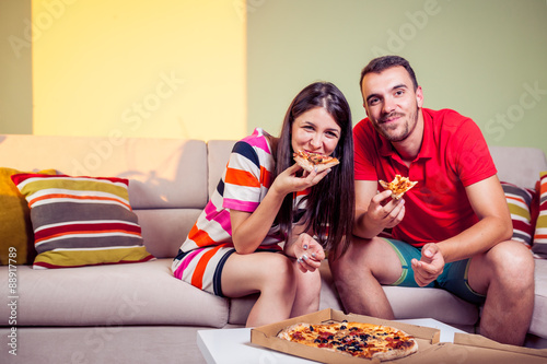 Funky young couple eating pizza on a couch