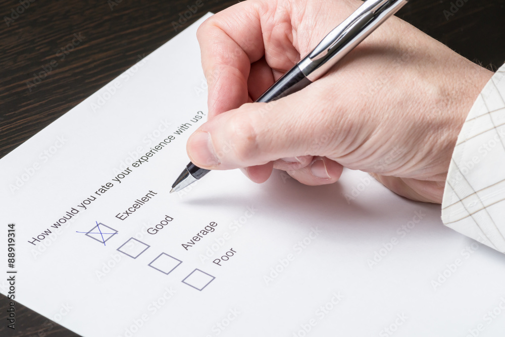 Close up of the hand of a business man filling out a customer satisfaction survey. Close up of the hand of a business man filling out a customer satisfaction survey.