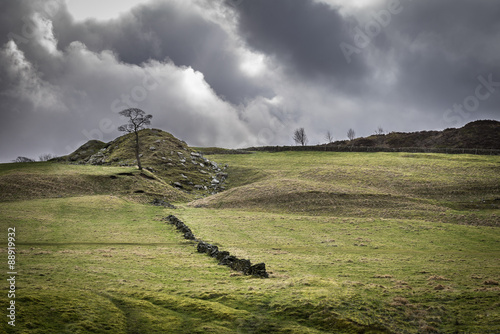 Dramatic landscape of the Yorkshire England countryside with stone wall, rocky mound and stormy clouds.
