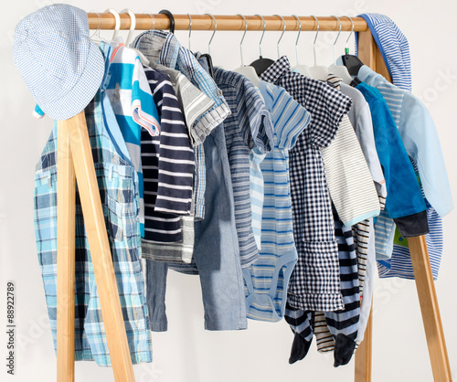 Dressing closet with clothes arranged on hangers.Blue and white wardrobe of newborn,kids, toddlers, babies full of all clothes.Many t-shirts,pants, shirts,blouses,blue hat, onesie hanging © iulianvalentin