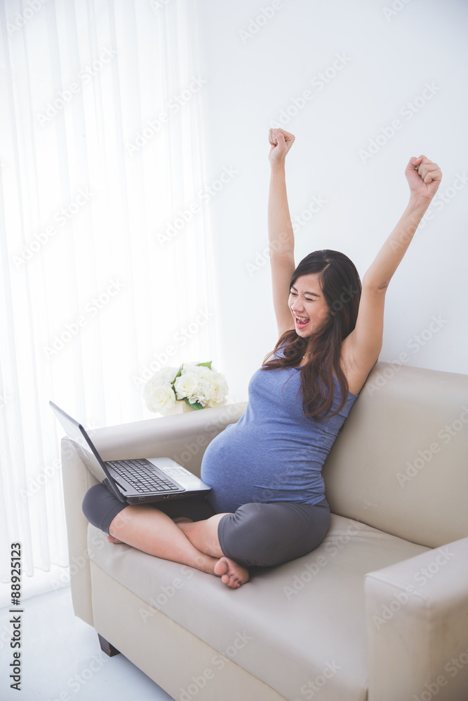 Beautiful pregnant asian woman sitting on the sofa with a laptop