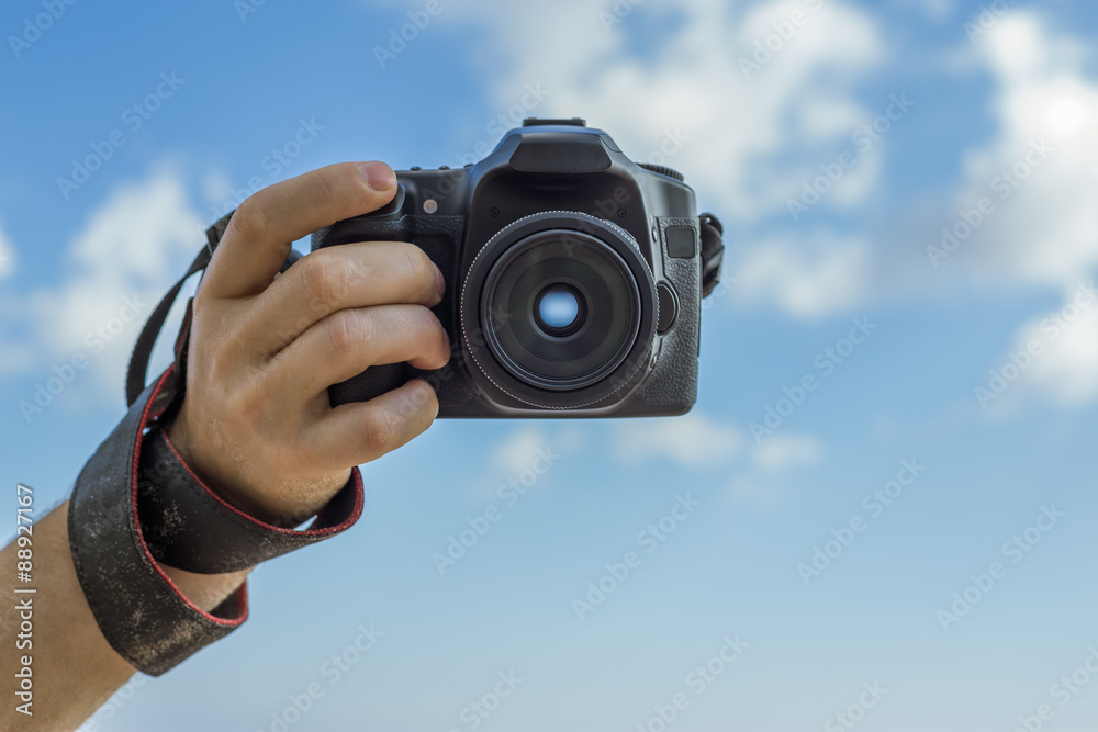 Photo for memory of summer holiday.. Man holding a camera on a background of blue sky with clouds.
