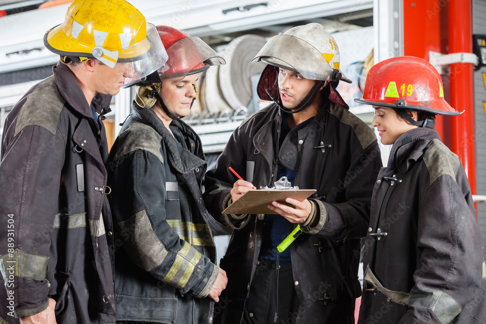 Obraz premium Team Of Firefighters Discussing Over Clipboard