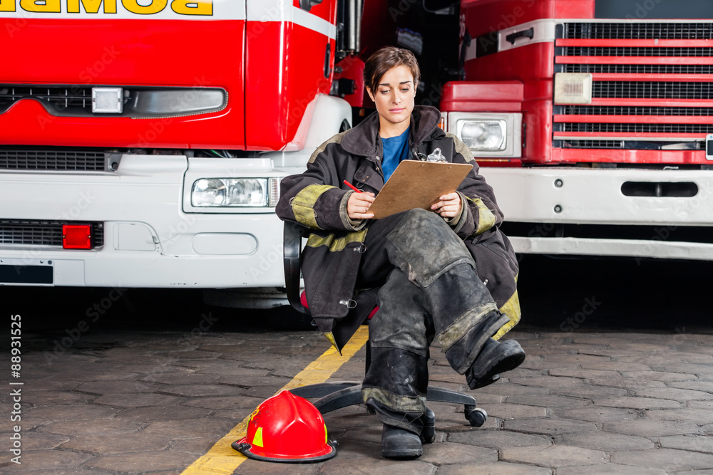 Obraz premium Firewoman Writing On Clipboard While Sitting Against Trucks