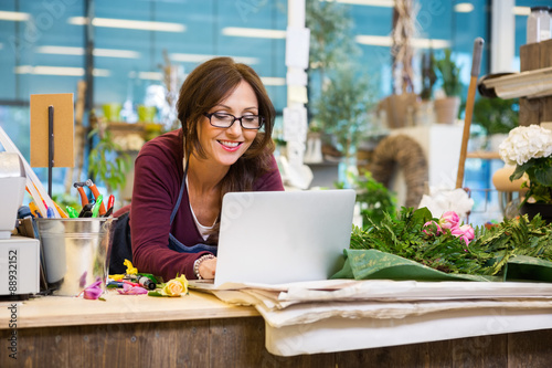 фотографія Happy Florist Using Laptop At Counter In Flower Shop
