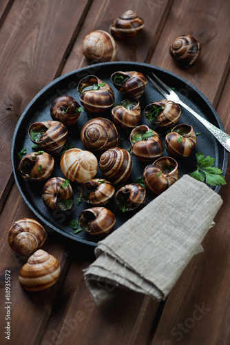 Baked snails with garlic butter and fresh parsley in a pan