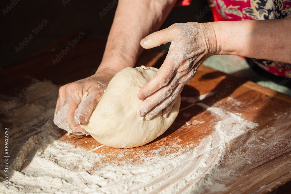 Senior woman hands knead dough on a table in her home kitchen