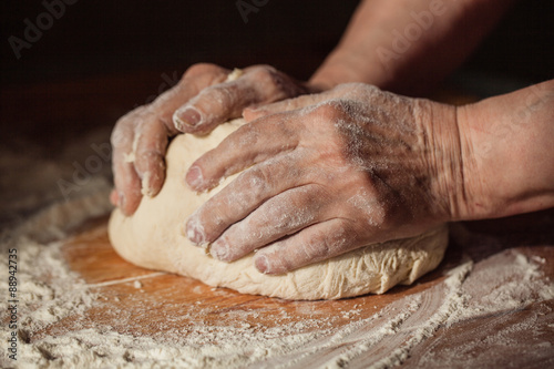 Billede på lærred Senior woman hands knead dough on a table in her home kitchen