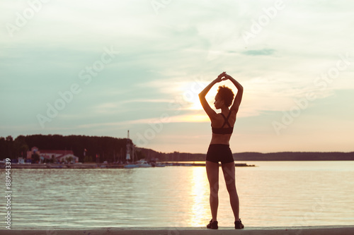 Attractive young African girl silhouette exercising stretching on a beach after running at sunset