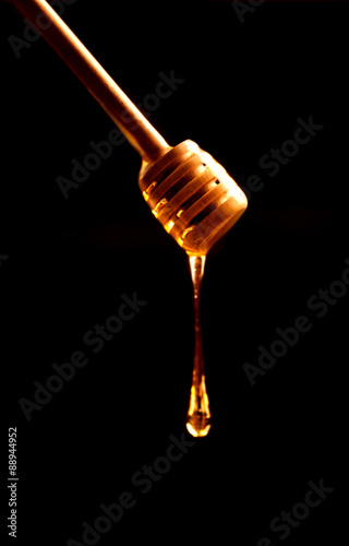 Honey stick with flowing honey over dark background close up
