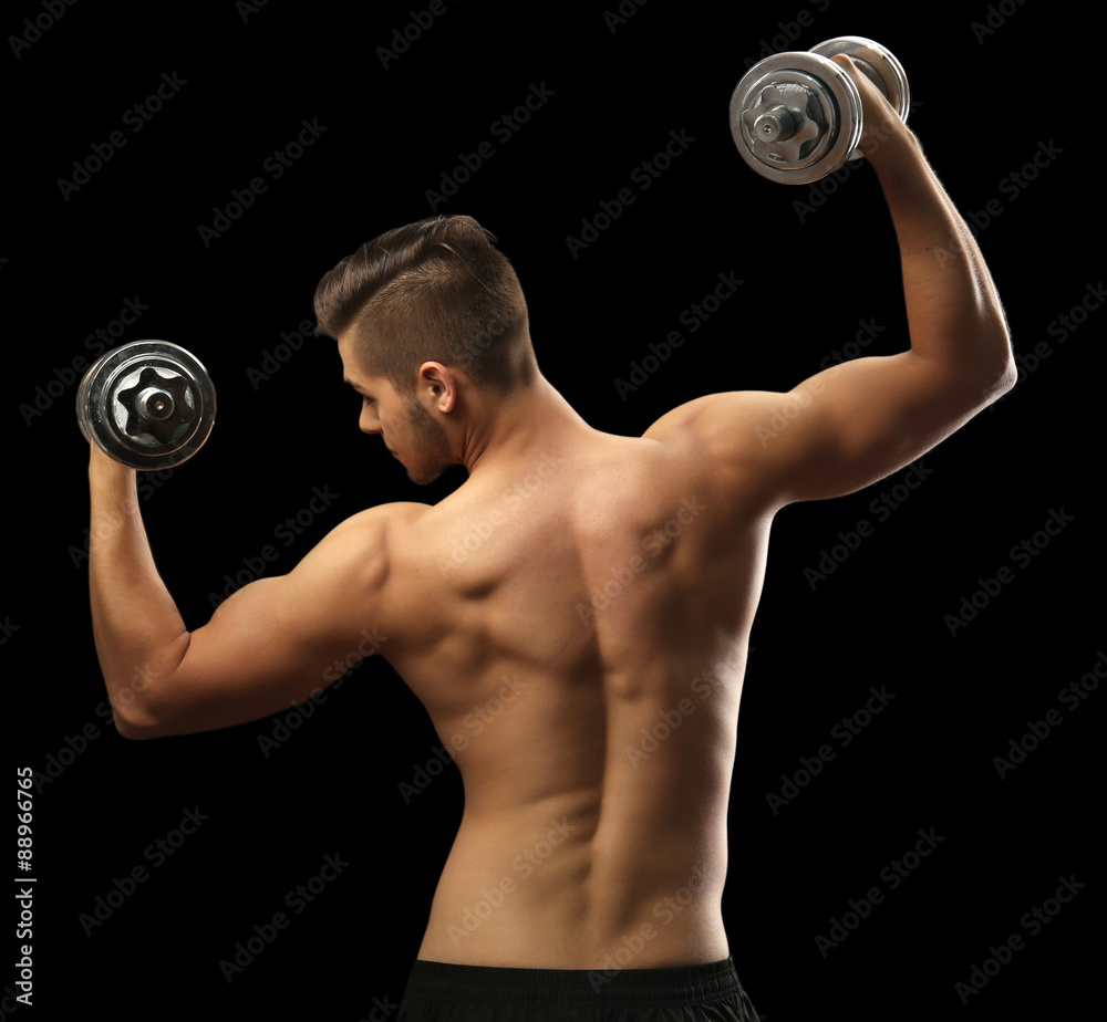 Muscle young man holding dumbbells on dark background Muscle young man holding dumbbells on dark background