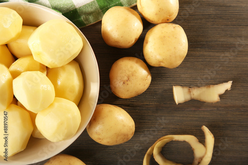 Peeled new potatoes in bowl on wooden table with napkin, top view