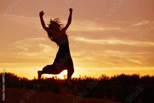 Silhouette of a beautiful girl jumping over sunset