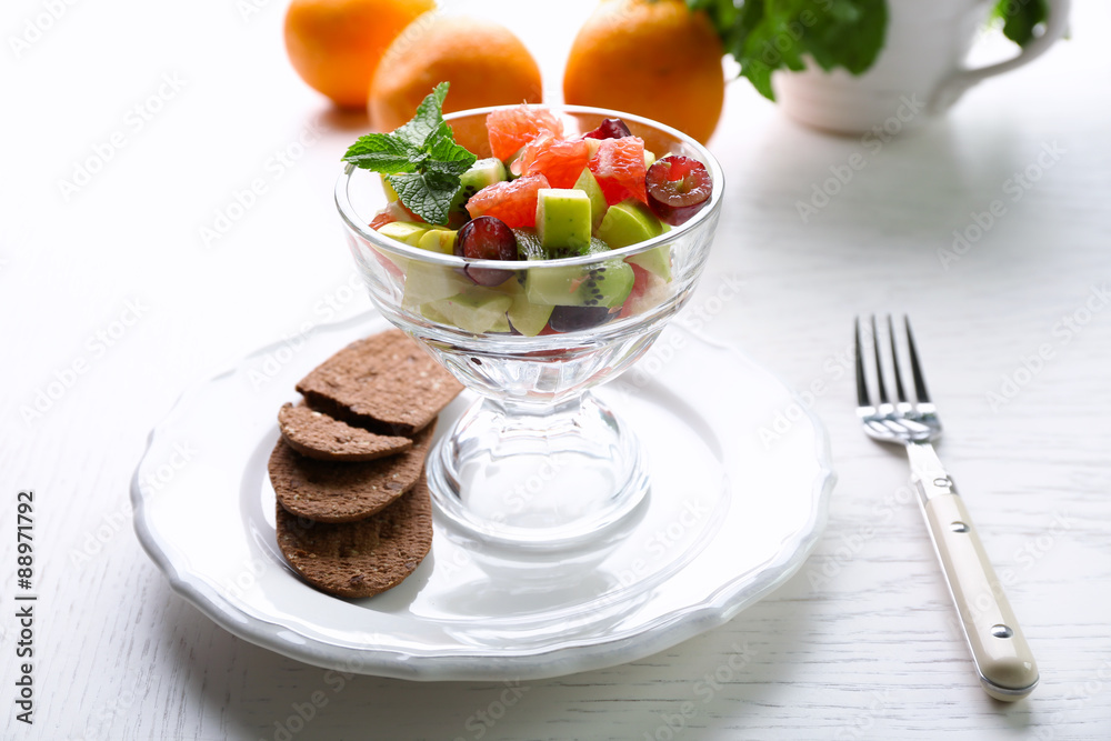 Fruit salad in glass bowl, on light wooden background