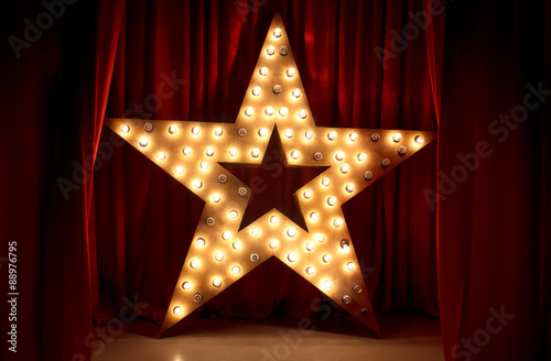 Obraz na płótnie Photo of golden star with light bulbs on red velvet curtain on stage