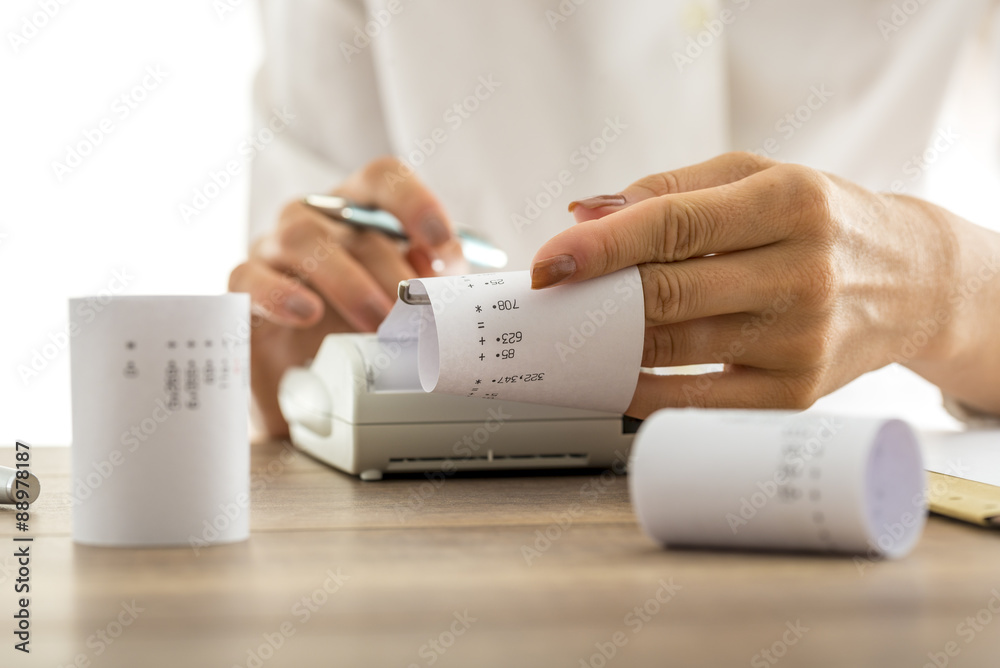 Woman doing calculations on an adding machine or calculator pulling off reams of paper with printed figures and totals, conceptual of accounting a bookkeeping, close up of her hands.