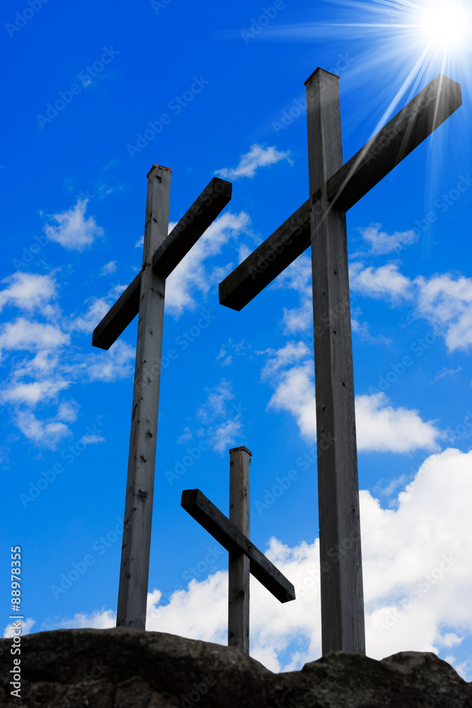 Golgotha - Three Crosses on Blue Sky. Three wooden crosses on a blue sky with clouds and sun rays on a hill. Symbol of Jesus crucifixion
