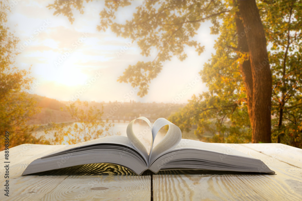 Obraz premium Open book on wooden table on natural blurred background. Heart book page. Back to school. Copy Space