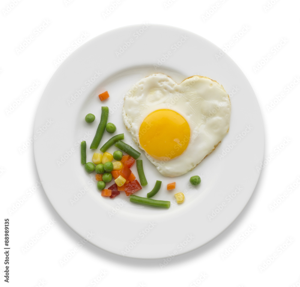 Fried egg in a shape of the heart and some vegetables on a white plate. Fried egg in a shape of the heart and some vegetables on a white plate.