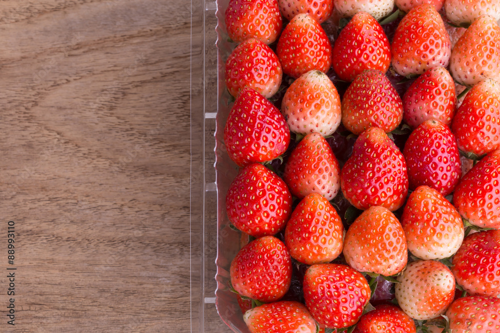 red ripe strawberry in plastic box of packaging on wood table