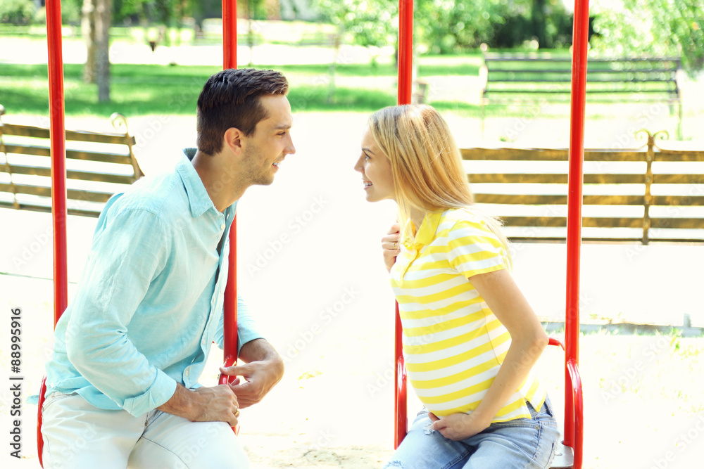 Obraz premium Young pregnant woman with husband on swing outdoors