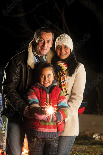 Young girl posing with a sparkler on bonfire night, with her parents