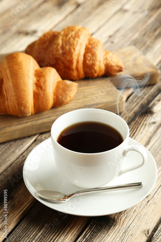 Tasty croissants with cup of coffee on brown wooden background
