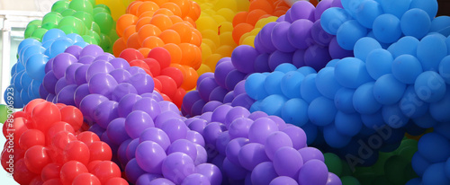 Groups of violet, blue, red, orange, yellow, green balloons together making cheerful colorful pile