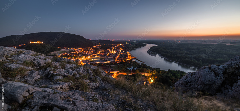 Fototapeta premium View of Lit Small City with River from the Hill at Sunset