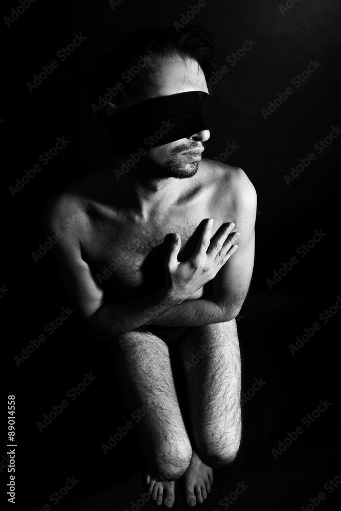 Seated handsome muscular man with a bandage over his eyes on a b Seated handsome muscular man with a bandage over his eyes on a b
