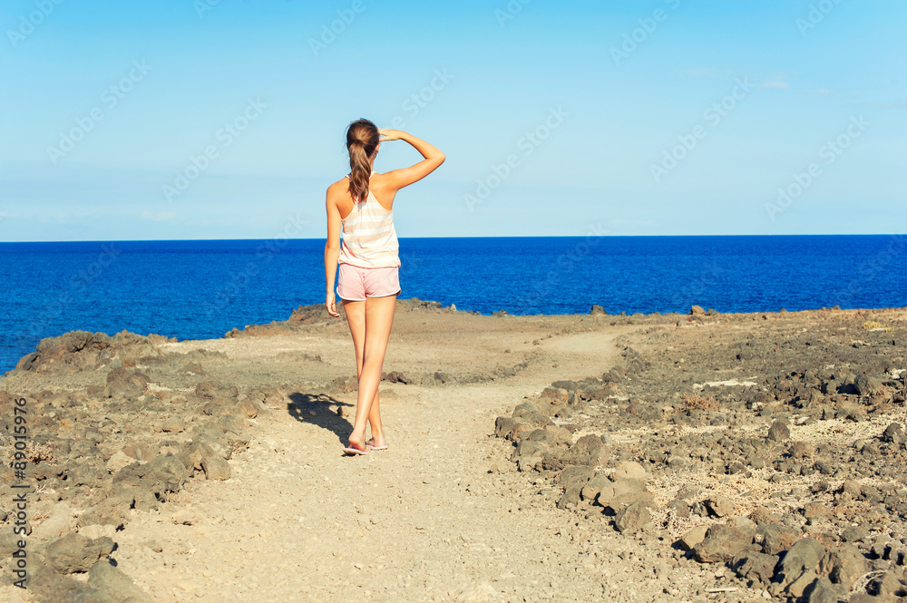 Young beautiful teenage girl walking on Atlantic ocean rock coas