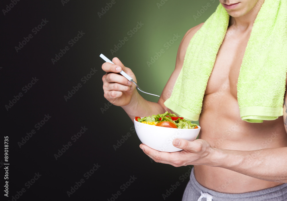 Strong fitness man holding a bowl of fresh salad on dark backgro Strong fitness man holding a bowl of fresh salad on dark backgro