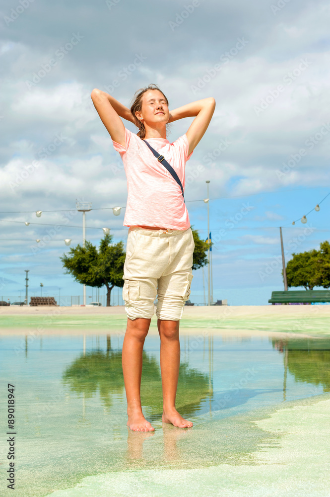 Hot summer in the city. Teenage barefoot girl standing in water