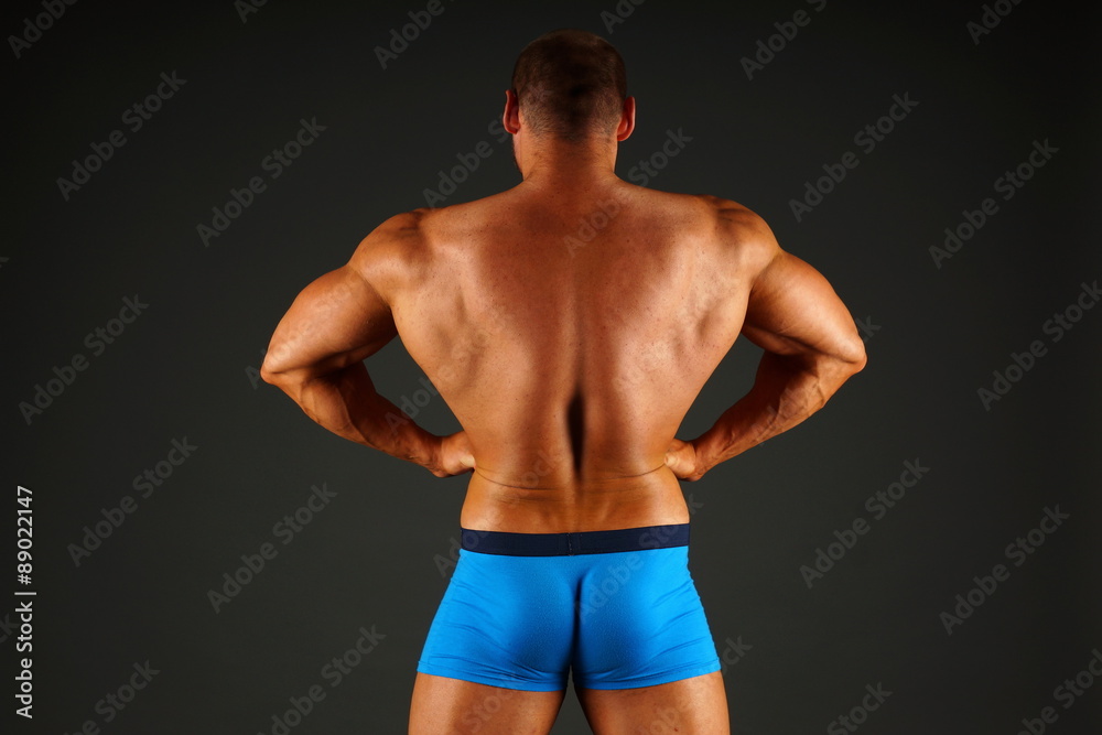 Big man shows his muscular back on gray background