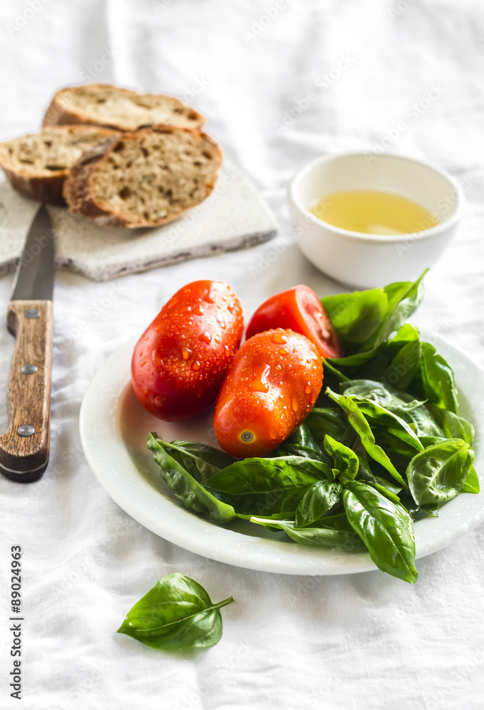 fresh Basil, tomatoes on a white plate, olive oil and a baguette on a white surface