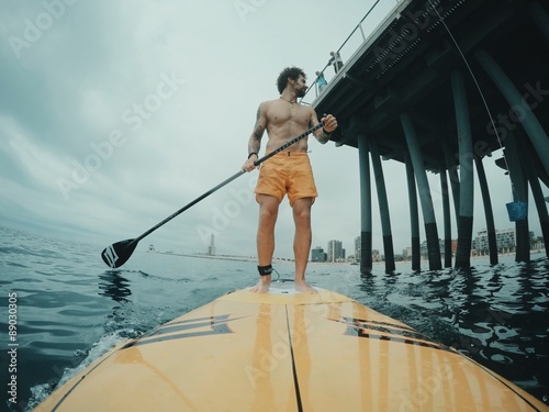surfer paddles around the big pier on his stand up paddle surf