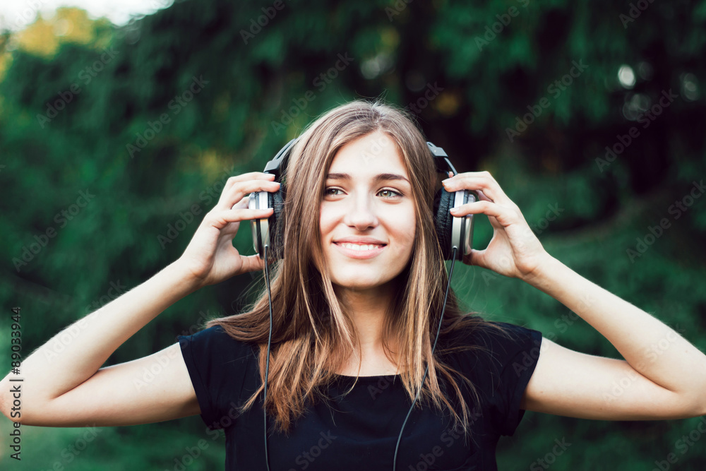 Beautiful young girl listening to music on headphones. The girl in the park .