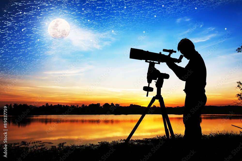 silhouette of young man looking through a telescope at the full