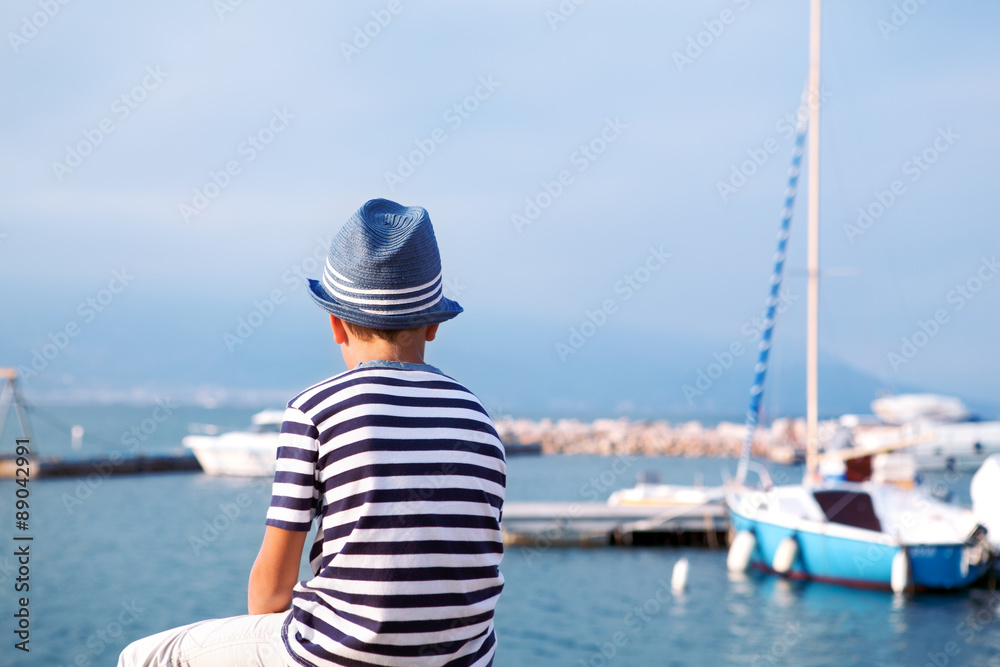 child in hat looking at sea and ship