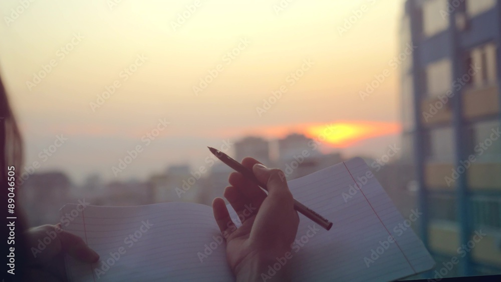 female hands with pen writing on notebook  at sunset in the city