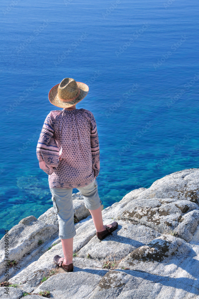 Woman standing on the rock near the sea and enjoying the beautiful blue sea color 