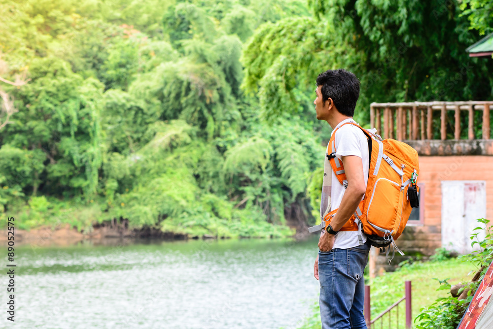 Man hiker in blue jean with orange backpack looking view of rive Man hiker in blue jean with orange backpack looking view of rive