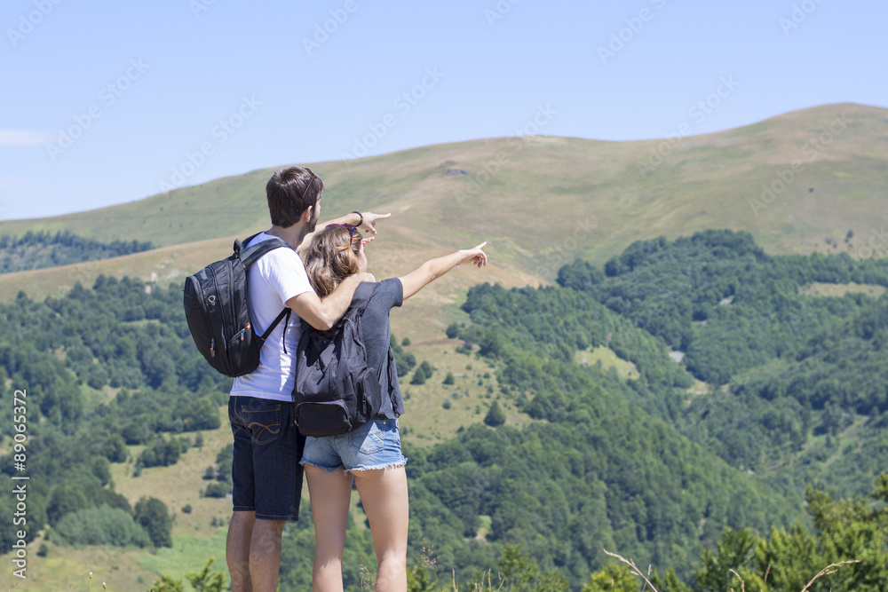 Couple of hikers with backpacks standing at viewpoint and enjoyi