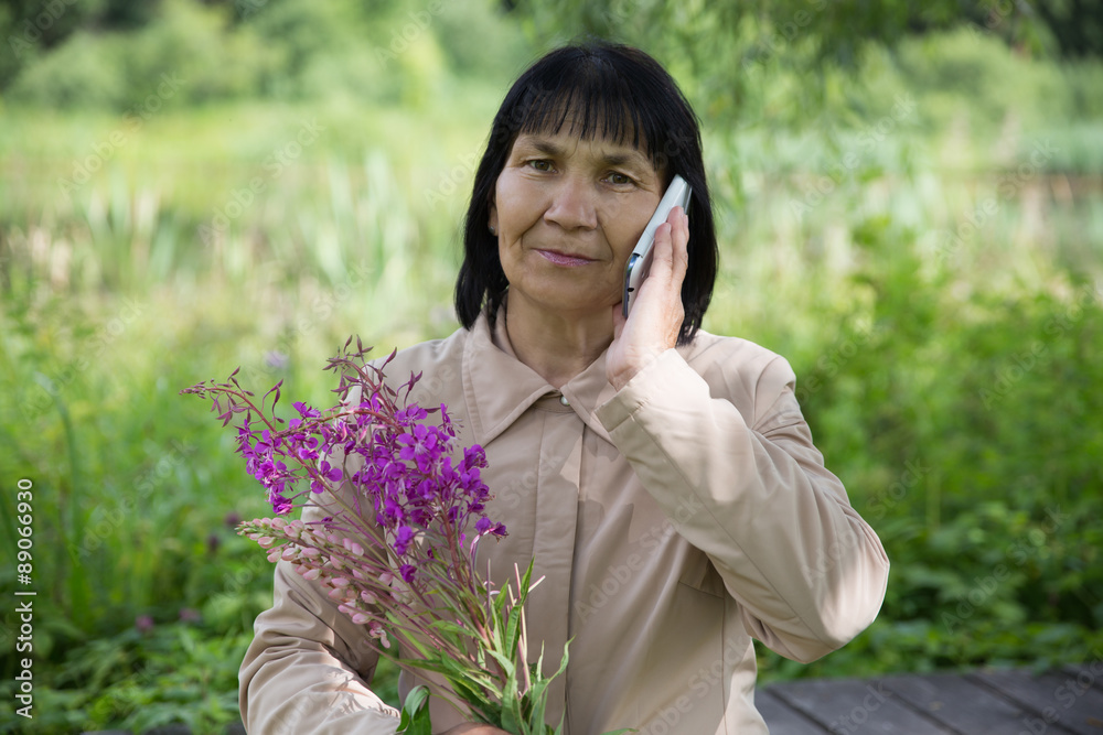 Senior Chuvash woman speaking by phone on summer green background Senior Chuvash woman speaking by phone on summer green background