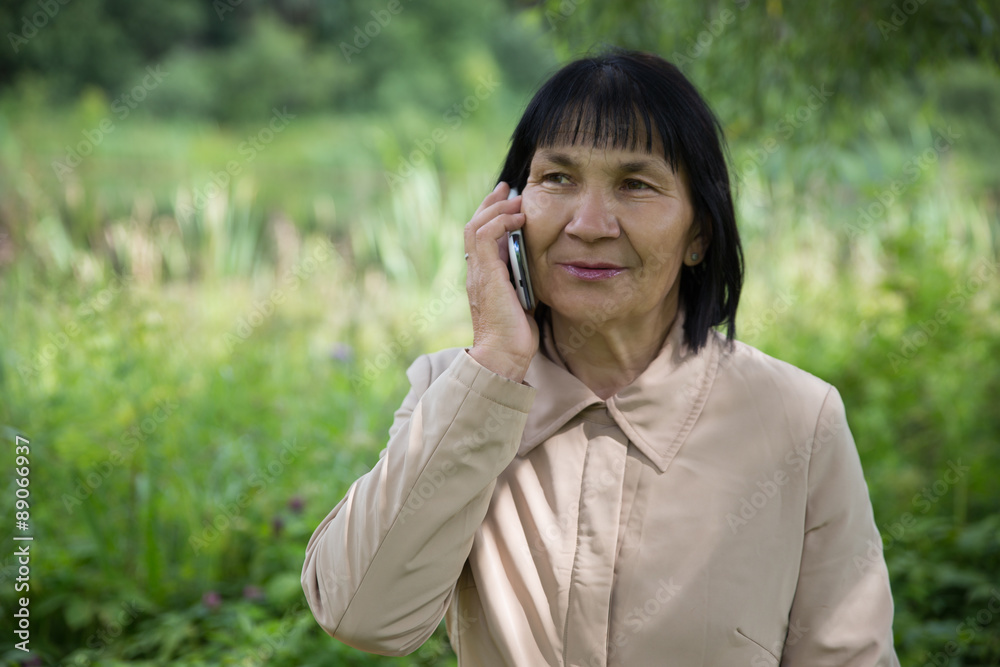 Senior Chuvash woman speaking by phone on summer green background Senior Chuvash woman speaking by phone on summer green background