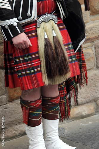 Scottish bagpiper dressed in kilt playing bag pipes, lower part with tartan skirt